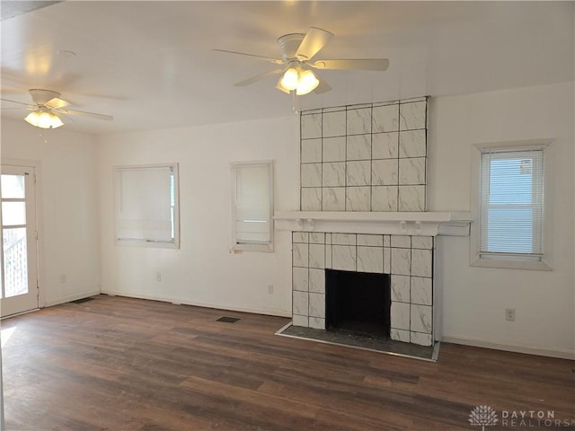 unfurnished living room featuring dark wood-type flooring, a tile fireplace, and a healthy amount of sunlight