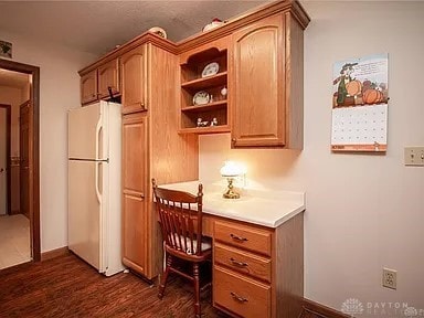 kitchen featuring white fridge, built in desk, and dark wood-type flooring