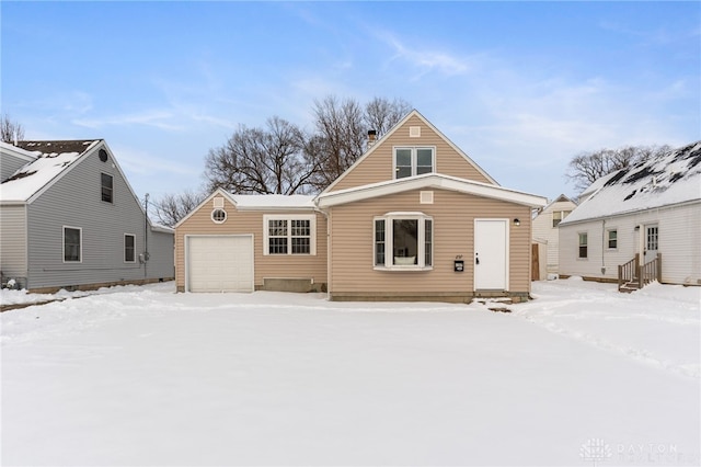 snow covered rear of property with a garage and an outbuilding