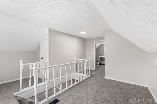 hall featuring lofted ceiling, carpet flooring, and a textured ceiling