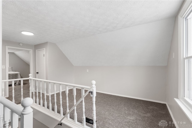 hall featuring vaulted ceiling, carpet flooring, and a textured ceiling