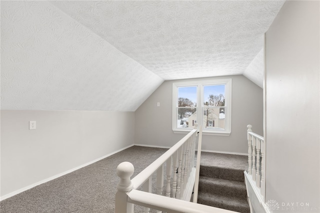 staircase with lofted ceiling, carpet floors, and a textured ceiling