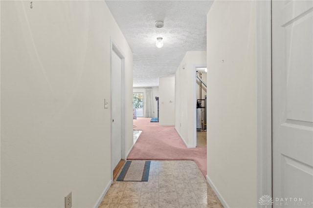 hallway with a textured ceiling and light colored carpet