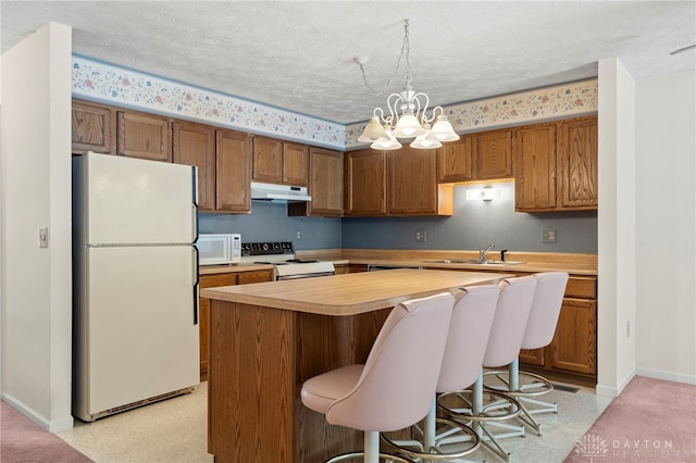 kitchen with hanging light fixtures, a notable chandelier, a textured ceiling, white appliances, and a kitchen island