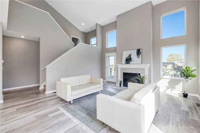 living room featuring a tiled fireplace, light hardwood / wood-style flooring, and a high ceiling