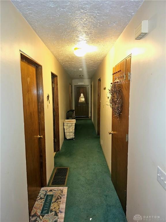 hallway with a textured ceiling and dark carpet