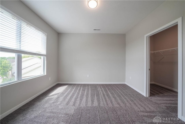 unfurnished bedroom with dark colored carpet, multiple windows, a spacious closet, and a closet