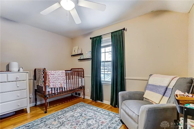 bedroom with ceiling fan, hardwood / wood-style floors, and a nursery area