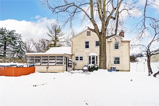 snow covered back of property featuring a hot tub, central AC unit, and a sunroom