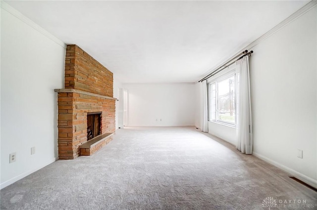 unfurnished living room with a stone fireplace, ornamental molding, and carpet floors