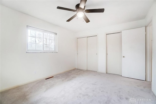 unfurnished bedroom featuring multiple closets, ceiling fan, and light colored carpet