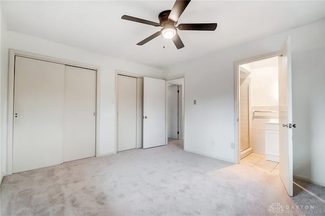 unfurnished bedroom with light carpet, connected bathroom, ceiling fan, and multiple closets