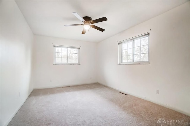 unfurnished room featuring ceiling fan, light carpet, and a wealth of natural light