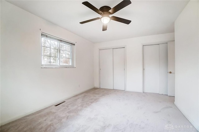 unfurnished bedroom featuring ceiling fan, light carpet, and two closets