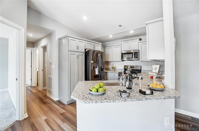 kitchen featuring light stone counters, light hardwood / wood-style flooring, kitchen peninsula, lofted ceiling, and appliances with stainless steel finishes