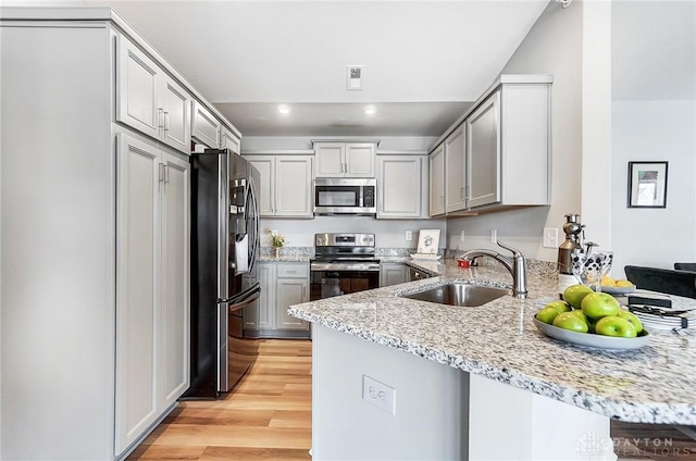 kitchen with sink, light hardwood / wood-style flooring, light stone counters, kitchen peninsula, and stainless steel appliances