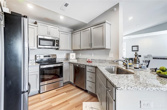 kitchen with lofted ceiling, sink, light hardwood / wood-style flooring, appliances with stainless steel finishes, and kitchen peninsula