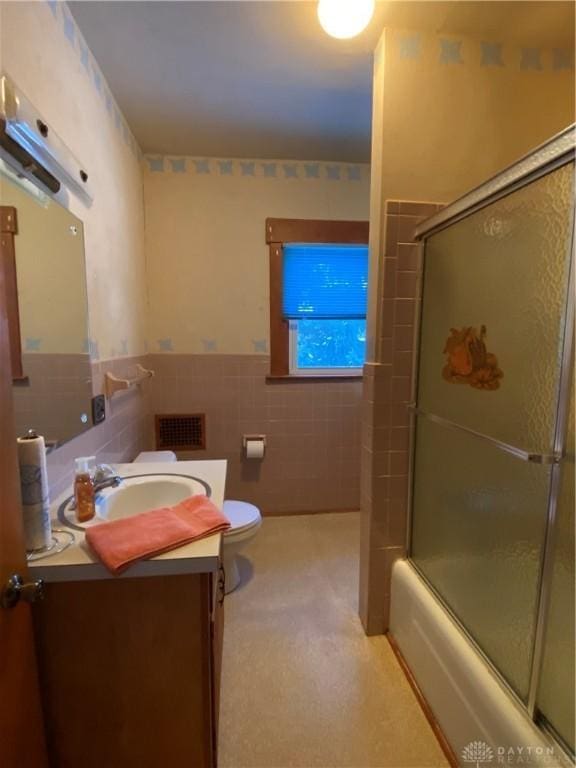 full bathroom featuring vanity, toilet, enclosed tub / shower combo, and tile walls