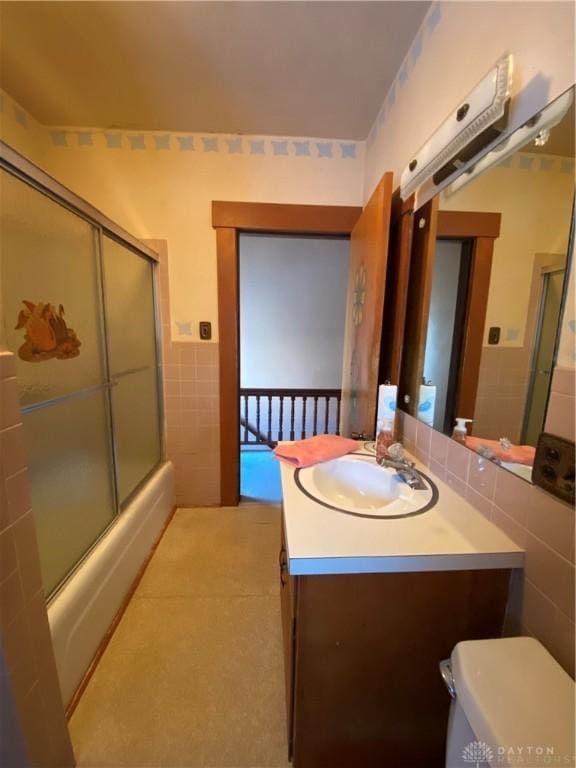 full bathroom featuring shower / bath combination with glass door, vanity, tile walls, and toilet