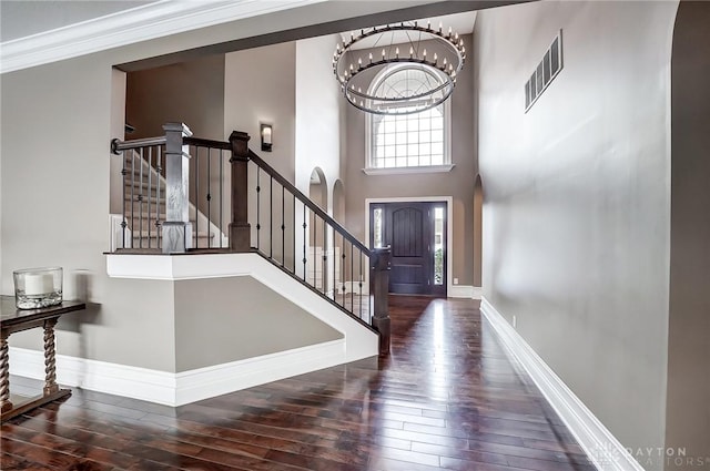 entrance foyer with a towering ceiling, ornamental molding, dark hardwood / wood-style flooring, and a notable chandelier