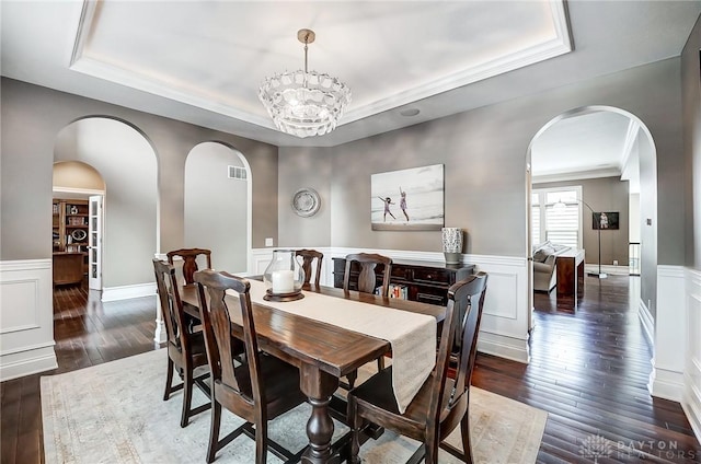 dining room with a tray ceiling, ornamental molding, dark wood-type flooring, and a notable chandelier