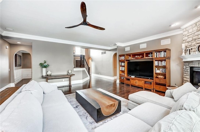 living room featuring a stone fireplace, ceiling fan, dark hardwood / wood-style floors, and ornamental molding