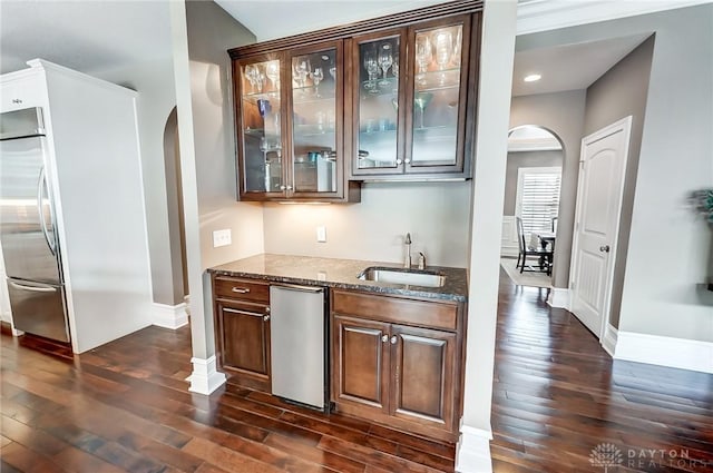 bar featuring sink, dark stone counters, and dark hardwood / wood-style floors