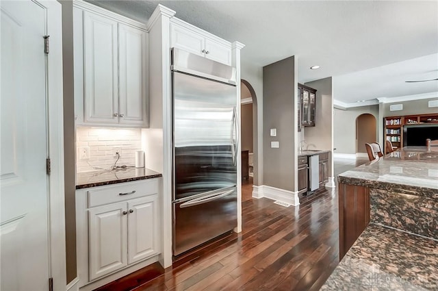 kitchen featuring white cabinets, stainless steel appliances, dark stone counters, and dark wood-type flooring