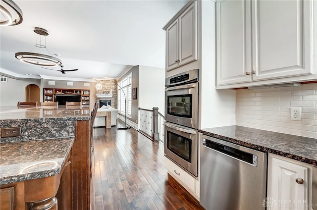 kitchen with dark stone counters, stainless steel appliances, ceiling fan, white cabinetry, and hanging light fixtures