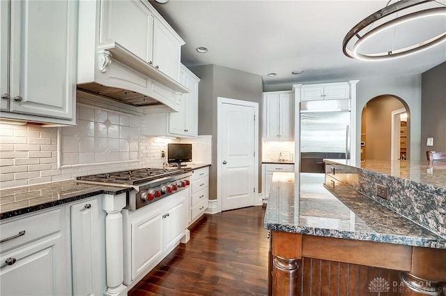 kitchen with white cabinets, dark hardwood / wood-style flooring, stainless steel appliances, and dark stone counters