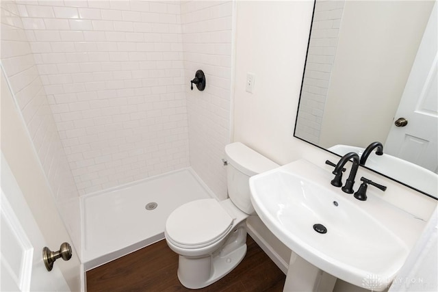 bathroom with tiled shower, hardwood / wood-style floors, toilet, and sink