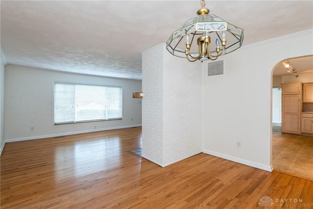 empty room with an inviting chandelier, ornamental molding, and light hardwood / wood-style flooring