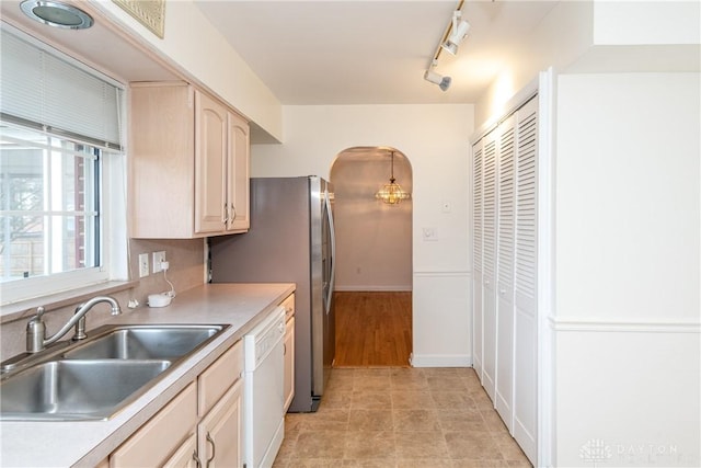 kitchen with white dishwasher, sink, rail lighting, light brown cabinetry, and decorative light fixtures