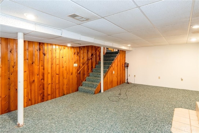 basement featuring carpet, a paneled ceiling, and wood walls