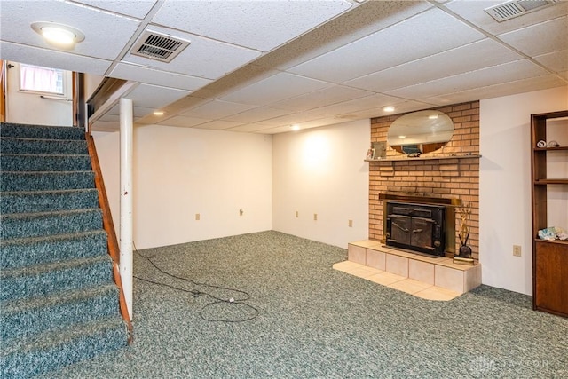 basement with a paneled ceiling, carpet floors, and a wood stove