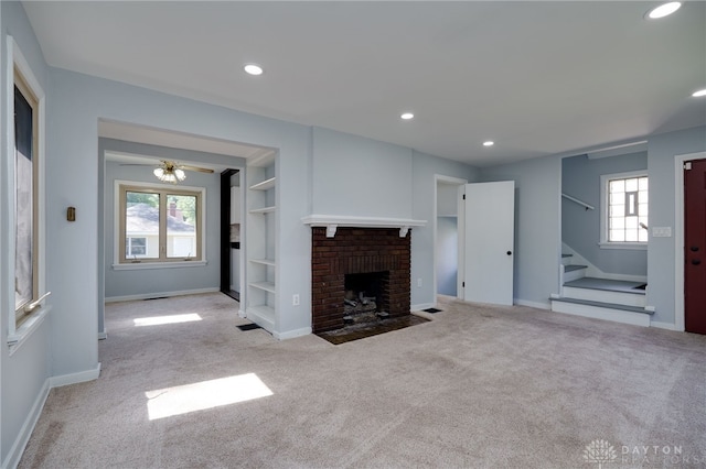 unfurnished living room with built in shelves, light colored carpet, a healthy amount of sunlight, and a brick fireplace