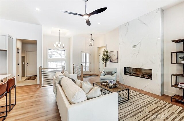 living room featuring ceiling fan with notable chandelier, light hardwood / wood-style flooring, and a premium fireplace