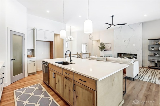 kitchen with white cabinetry, sink, a premium fireplace, stainless steel dishwasher, and an island with sink