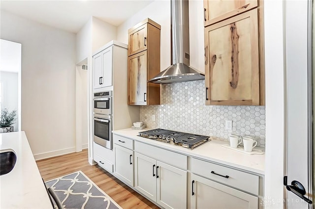 kitchen featuring white cabinets, wall chimney exhaust hood, appliances with stainless steel finishes, and light hardwood / wood-style flooring