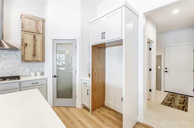 kitchen featuring decorative backsplash, light hardwood / wood-style flooring, stainless steel gas stovetop, and wall chimney range hood