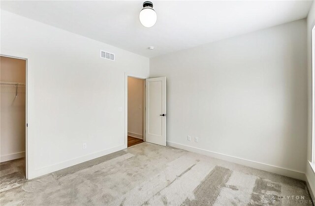 unfurnished bedroom featuring a walk in closet, light carpet, and a closet