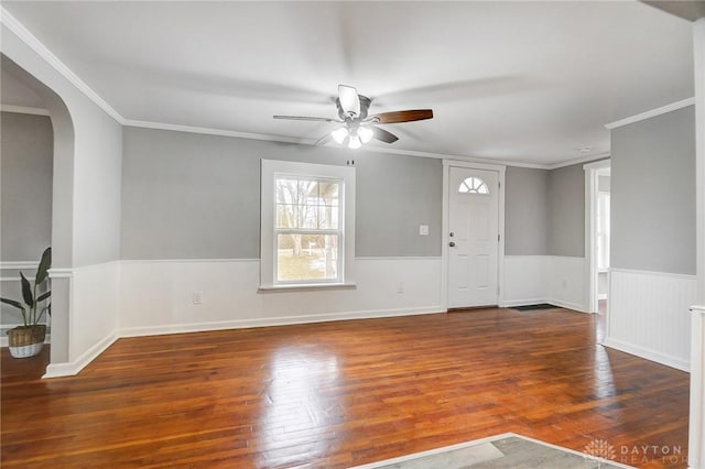 interior space featuring arched walkways, ceiling fan, a wainscoted wall, dark wood finished floors, and crown molding