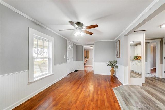 spare room with light wood-style floors, wainscoting, crown molding, and ceiling fan