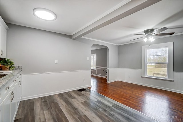 unfurnished room with a wainscoted wall, crown molding, arched walkways, and dark wood-type flooring