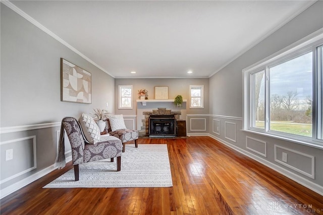 sitting room featuring ornamental molding, wood finished floors, a fireplace, a decorative wall, and recessed lighting