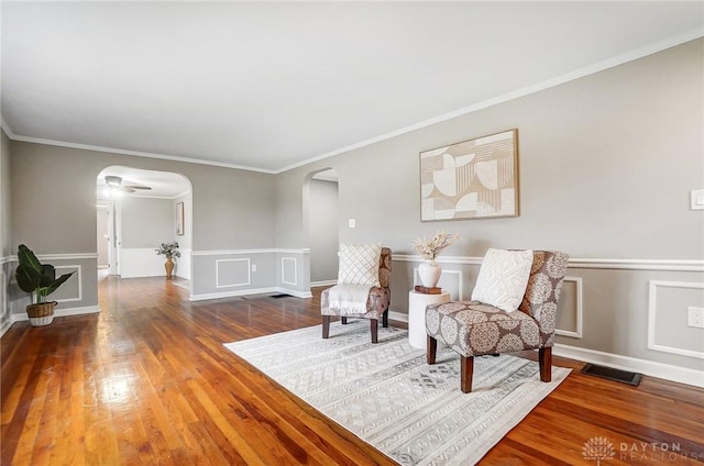 sitting room featuring arched walkways, wainscoting, visible vents, and wood finished floors