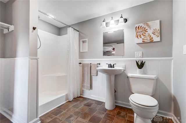 full bath featuring toilet, a wainscoted wall, curtained shower, stone finish flooring, and a sink