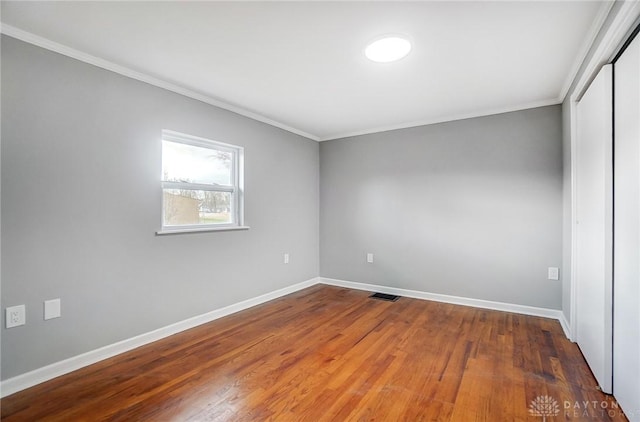 spare room featuring dark wood-style floors, crown molding, visible vents, and baseboards