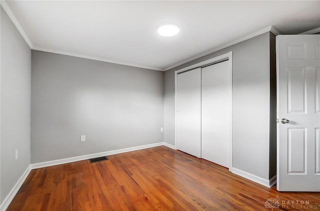 unfurnished bedroom featuring baseboards, visible vents, wood finished floors, and ornamental molding