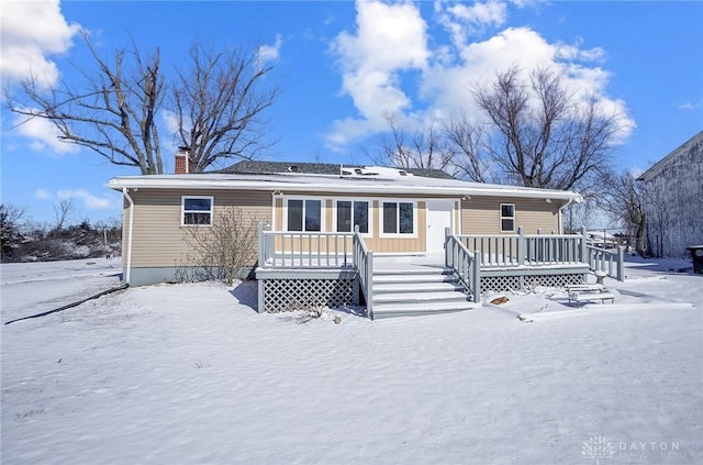 snow covered rear of property featuring a chimney and a wooden deck